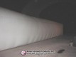Side view of a long white inflatable pitching dome inside a dark Sport Dome
