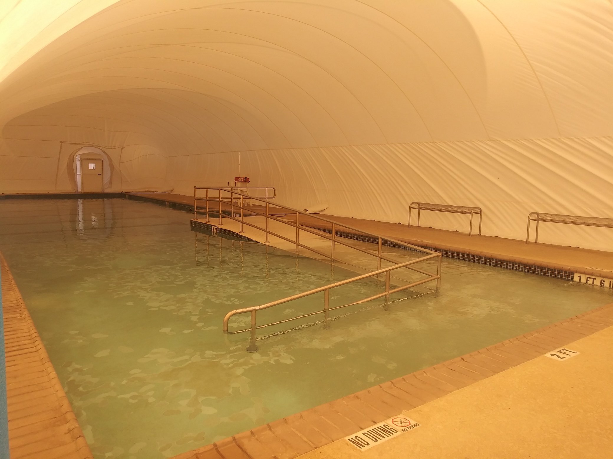 Accessible therapy pool with a ramp and handrails inside a white Ameri-Dome
